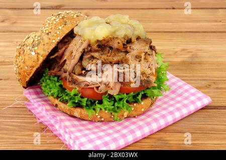 Sandwich au porc rôti de viande avec sauce aux pommes et salade dans un rouleau de pain couvert de graines sur fond de bois Banque D'Images