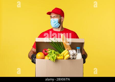 Livraison à emporter, quarantaine Covid-19 et concept d'épicerie. Le client commande une épicerie en ligne, le coursier se tord à l'appareil photo, apporter la boîte pleine de nourriture, portant Banque D'Images