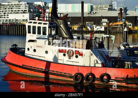 Bateau à remorqueurs en acier avec coque rouge et cabine blanche sur une surface calme du port. Banque D'Images