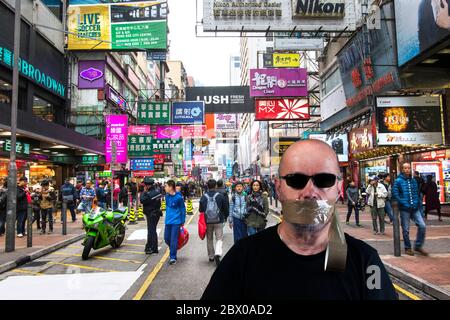 Un homme avec des lunettes dans une rue de Hong Kong avec sa bouche recouverte de ruban adhésif Banque D'Images