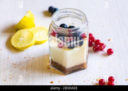 Sous vide Cheesecake dans un pot, photo de perspective du dîner avec coin de citron et garniture de baies, fond clair. Banque D'Images