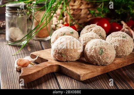 Boulettes de viande crues roulées dans un pain croustillant sur une planche à découper préparée pour la cuisson Banque D'Images