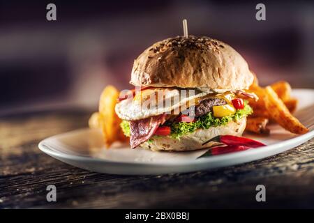 Hamburger de bœuf avec œuf frit, bacon, fromage, laitue et poivrons dans un pain au sésame avec des quartiers de pommes de terre avec paprika fumé et un piment extra frais sur le Banque D'Images