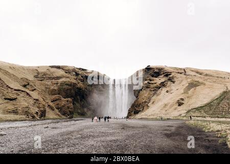 Cascade de Skogafoss dans le sud de l'Islande, sur l'anneau doré. Les visiteurs sont venus voir la cascade, les touristes marchent au pied de la montagne. Banque D'Images