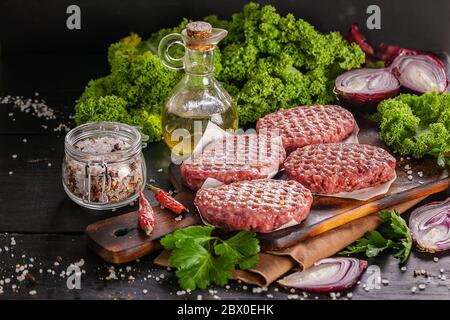 Côtelettes de hamburger crues faites de viande biologique. La nourriture reste encore en vie sur fond de bois sombre Banque D'Images