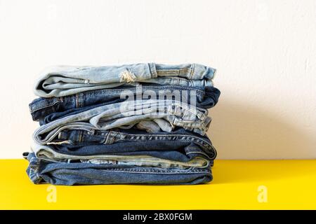 Une pile de jeans différents pantalons gros plan sur fond jaune et blanc, vêtements décontractés Banque D'Images