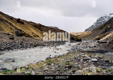 Vue panoramique sur la vallée en Islande. La rivière de montagne peu profonde coule à travers la gorge avec la toile de fond des montagnes avec l'herbe jaune et Banque D'Images