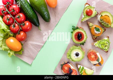 Des légumes entiers et des sandwiches végétariens avec tomates, avocat, concombre, verdness, fromage, olive sont posés sur des morceaux de papier d'emballage sur le dos vert Banque D'Images