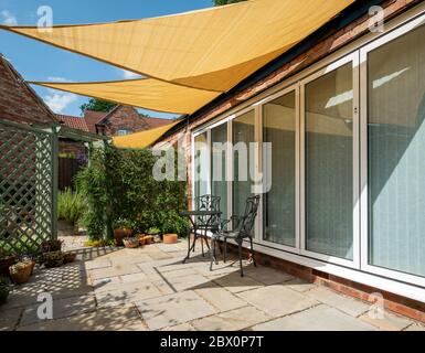 Petit jardin patio avec des parasols jaunes, triangulaires et bleu ciel au-dessus d'un soleil d'été, Angleterre, Royaume-Uni Banque D'Images