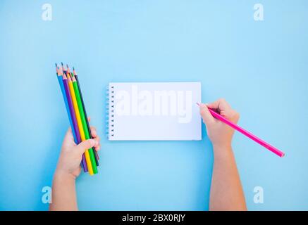 Child's hands holding colorful crayons et un ordinateur portable sur fond bleu avec copyspace. Mise à plat de style. Concept Retour à l'école. Banque D'Images