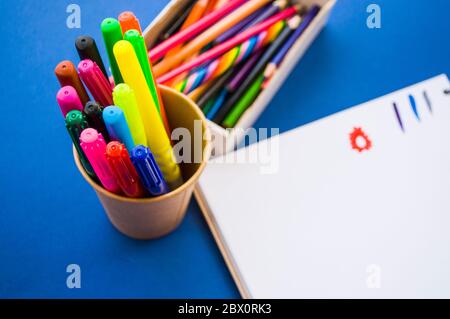 Les mains des enfants dessinant avec des crayons et des marqueurs colorés dans un carnet sur fond bleu. Style de pose à plat. Concept de retour à l'école. Banque D'Images