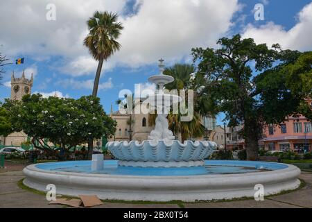 Bridgetown, Barbade, Caraïbes - 22 septembre 2018 : Fontaine devant le Parlement avec drapeau et horloge sur la tour. Nuages blancs dans le ciel bleu Banque D'Images