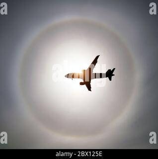 Silhouette d'un avion dans le ciel soleil et halo dans les nuages Banque D'Images