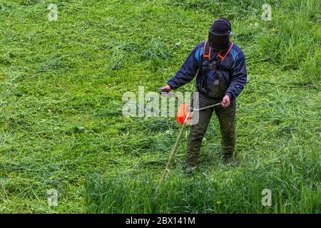 tondeuse homme avec tondeuse à ficelle et masque de visage trimmong herbe - gros plan Banque D'Images