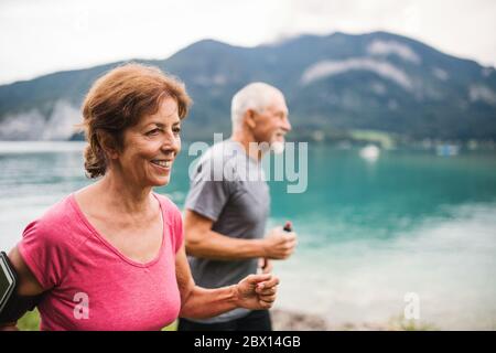 Couple de retraités senior avec smartphone fonctionnant au bord du lac dans la nature. Banque D'Images