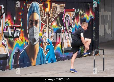 Un coureur s'arrête à côté d'une fresque montrant le personnel médical portant un équipement de protection individuelle (EPI) à Shoreditch, dans l'est de Londres, après l'introduction de mesures pour faire sortir l'Angleterre du confinement. Banque D'Images