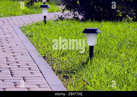 Éclairage du jardin - éclairage de la batterie solaire sur une pelouse verte à côté d'un chemin pavé Banque D'Images