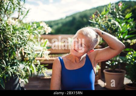 Une femme âgée debout à l'extérieur sur une terrasse en été, en s'étirant. Banque D'Images