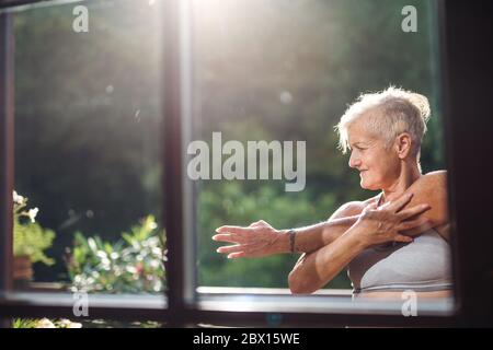 Femme âgée avec soutien-gorge de sport s'étendant à l'extérieur sur une terrasse en été. Banque D'Images