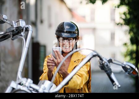 Une femme âgée et gaie voyageant en ville avec une moto, prenant un selfie. Banque D'Images