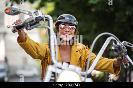 Femme âgée et gaie voyageant en ville avec une moto. Banque D'Images