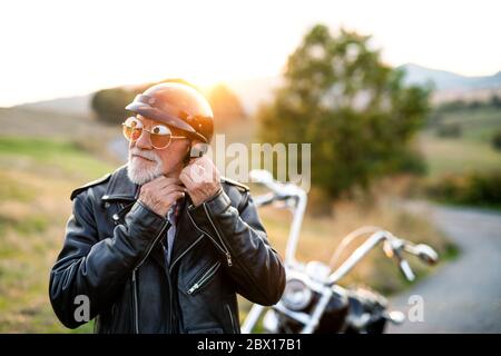 Un homme âgé voyageant avec moto à la campagne, mettant un casque. Banque D'Images