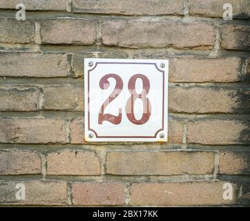 Numéro de maison 28 vingt-huit. Numéros bruns sur une plaque blanche construite sur un vieux mur de briques Banque D'Images