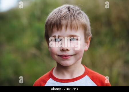 Un portrait d'un garçon d'école debout dans la nature, regardant l'appareil photo. Banque D'Images