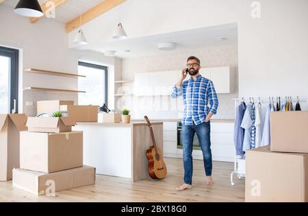 Homme mature avec des boîtes se déplaçant dans une nouvelle maison, à l'aide d'un smartphone. Banque D'Images