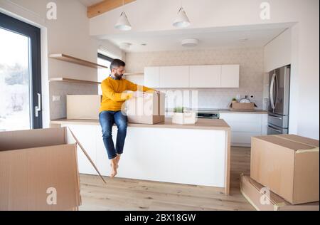 Homme mature avec des boîtes se déplaçant dans une nouvelle maison non meublée, déballage. Banque D'Images