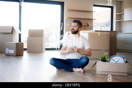 Homme mature avec café et boîtes se déplaçant dans la nouvelle maison, déballage. Banque D'Images