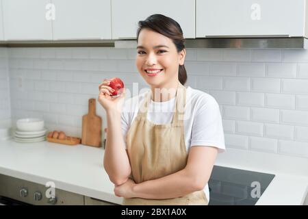 Les femmes asiatiques portent un tablier posé dans la cuisine à la maison regardant l'appareil photo, pomme rouge à la main Banque D'Images