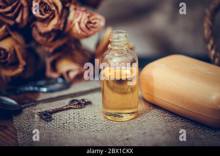 Huile essentielle de neroli dans une bouteille de verre avec des fleurs séchées sur fond de bois texturé ancien. Mise au point sélective. Banque D'Images