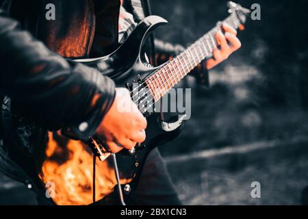 Gros plan des flammes sur le corps d'une guitare électrique noire dans la nuit Banque D'Images