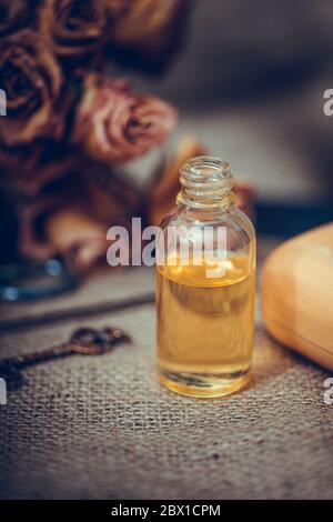 Huile essentielle de neroli dans une bouteille de verre avec des fleurs séchées sur fond de bois texturé ancien. Mise au point sélective. Banque D'Images