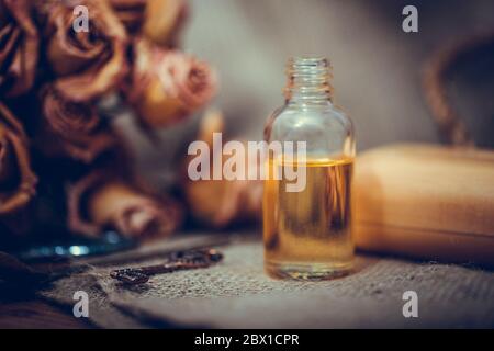 Huile essentielle de neroli dans une bouteille de verre avec des fleurs séchées sur fond de bois texturé ancien. Mise au point sélective. Banque D'Images