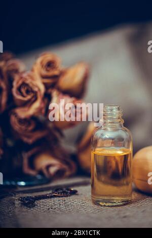 Huile essentielle de neroli dans une bouteille de verre avec des fleurs séchées sur fond de bois texturé ancien. Mise au point sélective. Banque D'Images