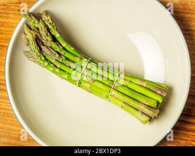 Un bouquet d'asperges dans un bol sur une planche à découper en bois Banque D'Images