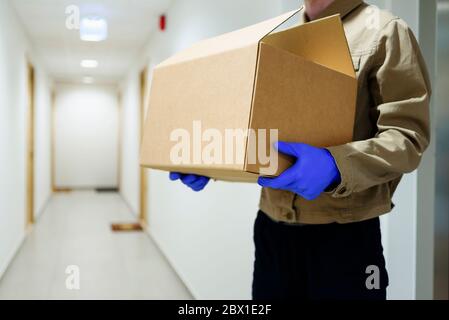 Liveur avec boîte en carton dans le couloir près de la porte. Utilisation de gants de protection en quarantaine Banque D'Images