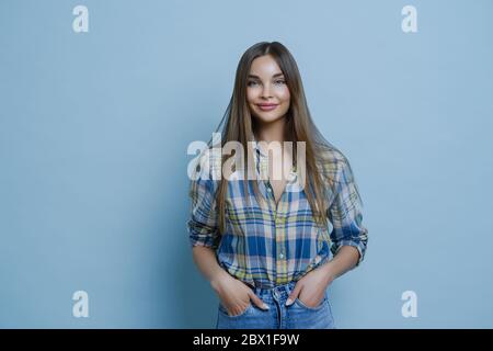 Attrayant étudiant heureux de parler de travail à temps partiel, garde les mains dans les poches de jeans, étant heureux en raison de nouvelles positives, a le sourire agréable, isola Banque D'Images