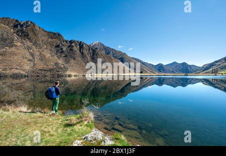 Randonneur debout au bord d'un lac, montagnes reflétées dans le lac, Moke Lake près de Queenstown, Otago, South Island, Nouvelle-Zélande Banque D'Images