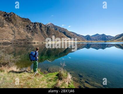 Randonneur debout au bord d'un lac, montagnes reflétées dans le lac, Moke Lake près de Queenstown, Otago, South Island, Nouvelle-Zélande Banque D'Images