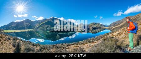 Panorama, randonneur debout sur une pierre, montagnes reflétées dans un lac, Moke Lake près de Queenstown, Otago, South Island, Nouvelle-Zélande Banque D'Images