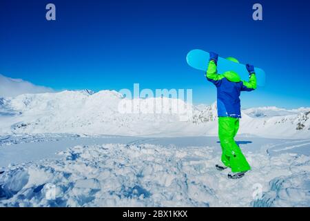 Portrait arrière d'un garçon tenir le snowboard sur les épaules se tenir dans la neige sur la montagne vue de haut de gamme sur l'arrière-plan Banque D'Images