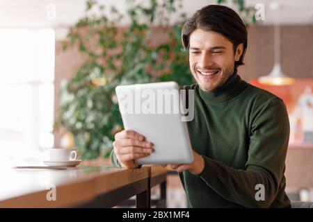 Homme joyeux qui passe des appels vidéo via une tablette numérique, intérieur d'un café Banque D'Images