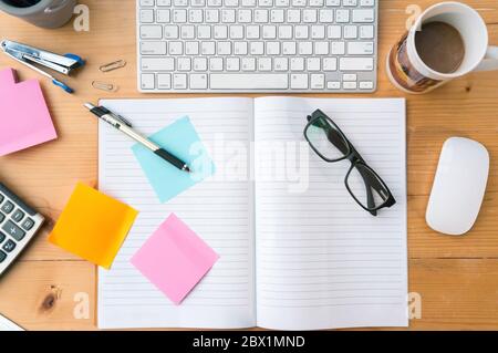 Vue de dessus sur le carnet ouvert, note, tasse de café, clavier autre équipement sur bureau en bois. Banque D'Images