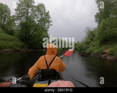 Les hommes dans un imperméable de couleur orange flottent sur un kayak sur la forêt rivière tranquille, le beau paysage, un temps pluvieux, s'entae activement avec un oar Banque D'Images