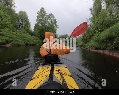 Les hommes dans un imperméable de couleur orange flottent sur un kayak sur la forêt rivière tranquille, le beau paysage, un temps pluvieux, s'entae activement avec un oar Banque D'Images