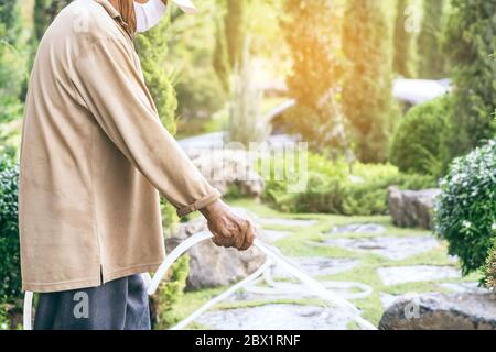 Un homme âgé en quarantaine porte un masque facial pour empêcher la propagation du virus Corona (Covid-19) arroser des plantes pour faire de l'exercice dans le jardin à la maison. Ne Banque D'Images