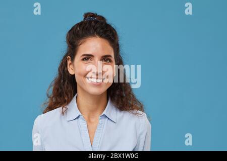 Portrait de jeune belle femme avec des cheveux bouclés souriant à l'appareil photo isolé sur fond bleu Banque D'Images